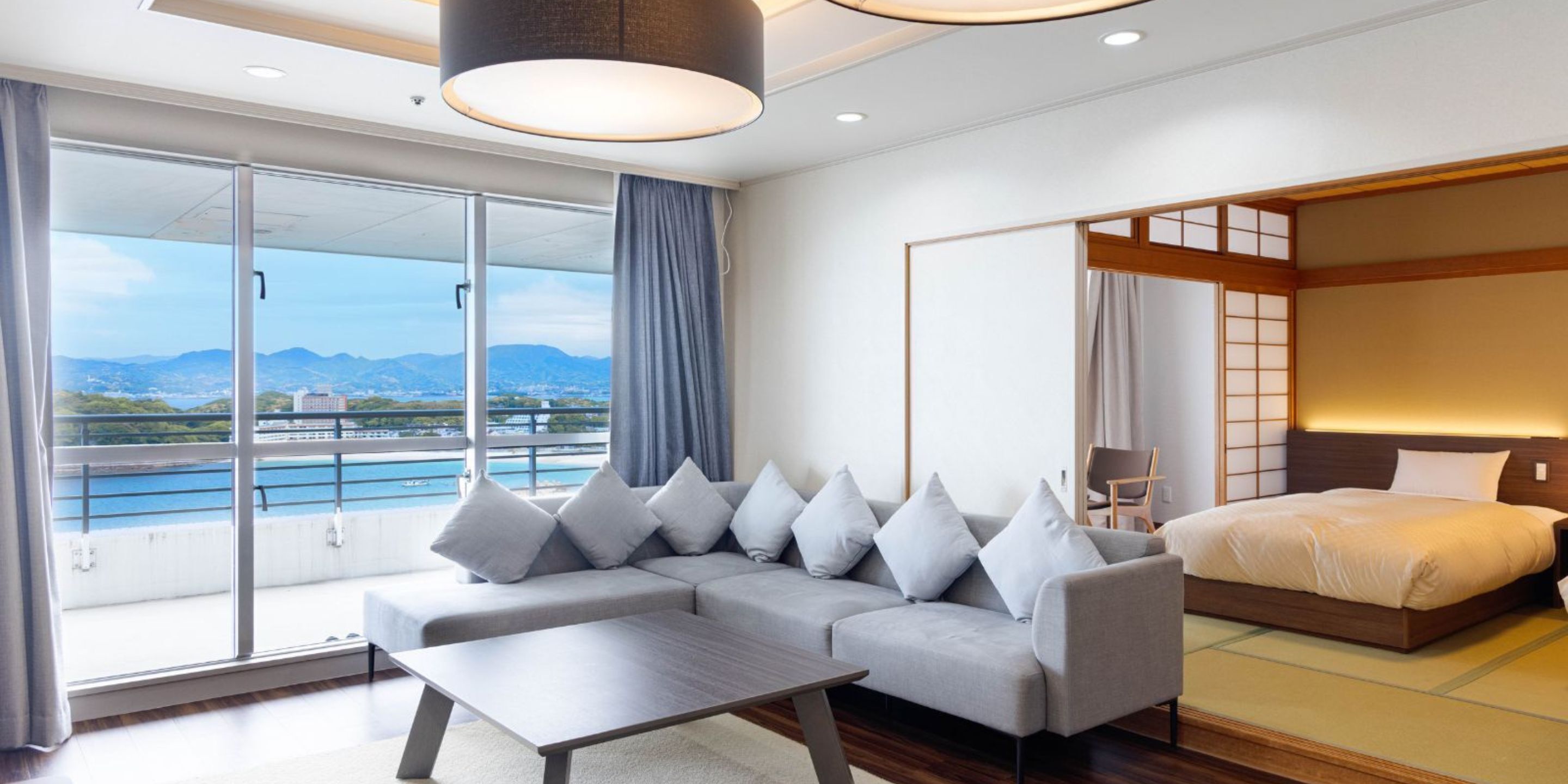 A modern hotel room with a sofa, a bed, a view of the sea, and a balcony.