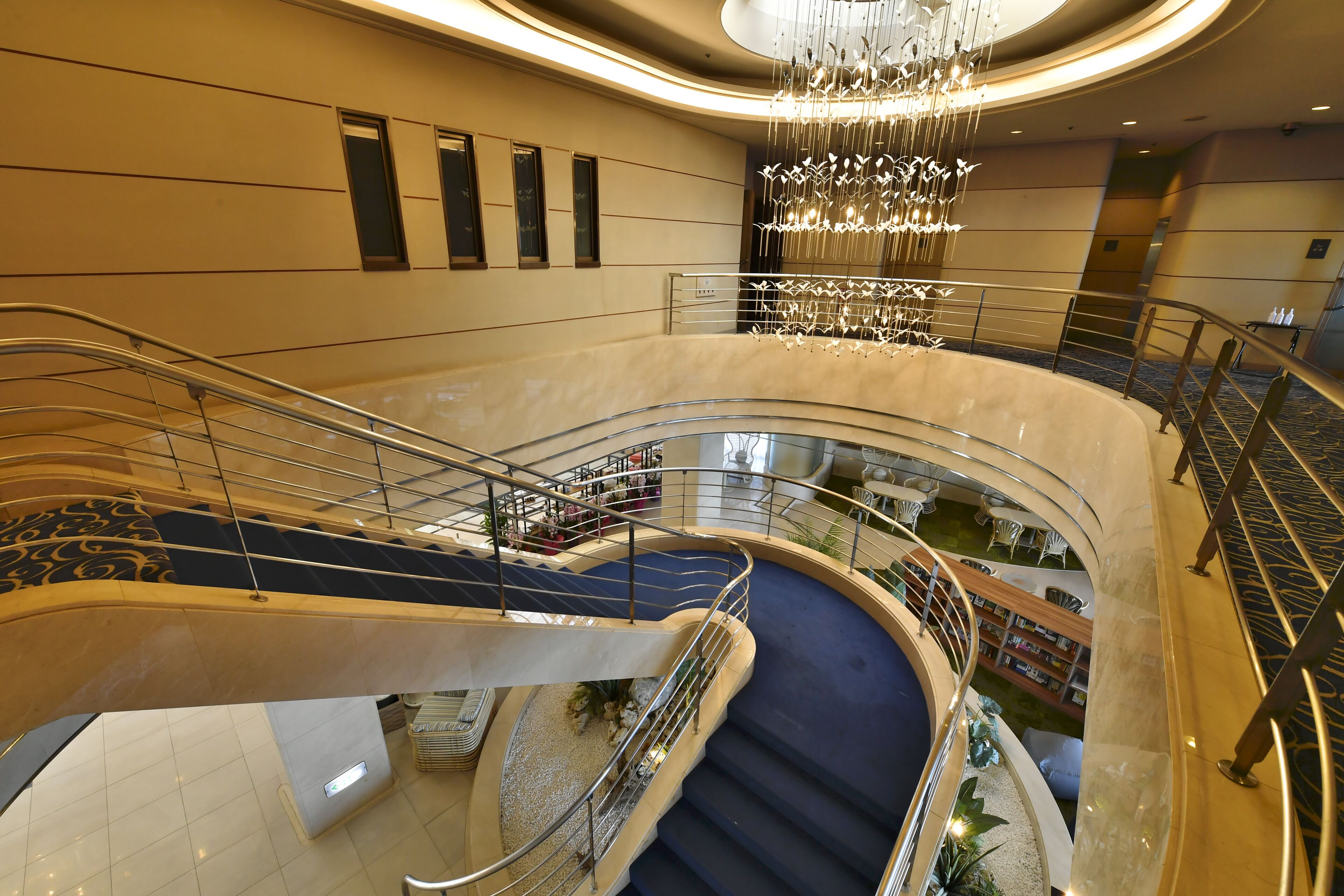 A multi-level atrium with a central staircase, glass railings, and a chandelier.