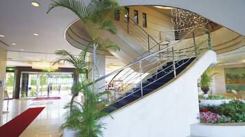 A modern hotel lobby with a curved staircase, potted plants, and a red carpet.