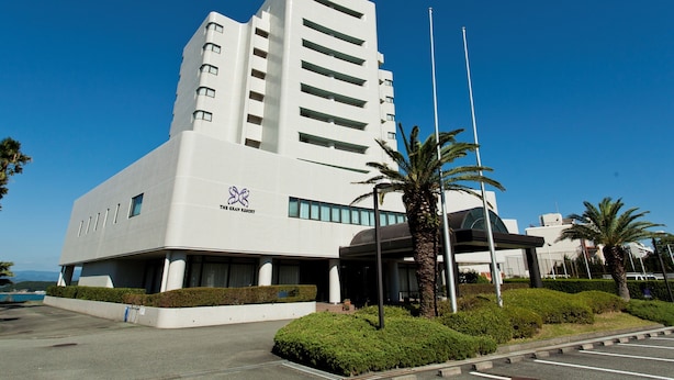 Un hotel moderno con fachada blanca, varios pisos y una entrada destacada, con una palmera en primer plano.
