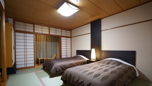 Et traditionelt japansk værelse med tatamimåtter, to senge med matchende sengetøj, en skydedør af shoji-skærm og et skrivebord med stol.