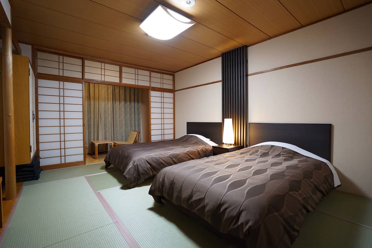 A traditional Japanese-style room with tatami flooring, two beds with matching bedding, a sliding shoji screen door, and a desk with a chair.