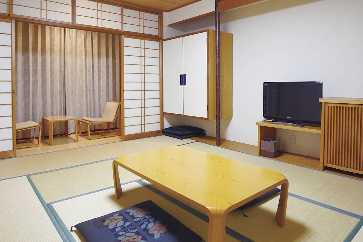 A traditional Japanese room with tatami flooring, a low table, a television, and sliding doors.