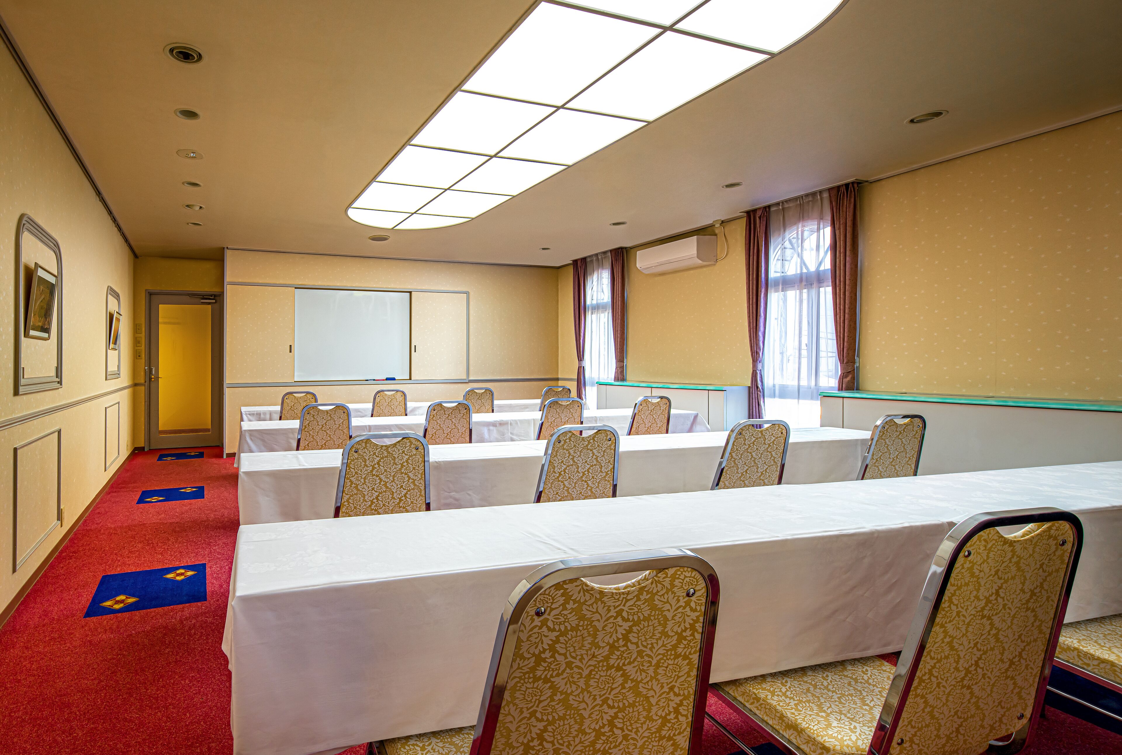A conference room with long tables and chairs, a whiteboard, and a red carpet.
