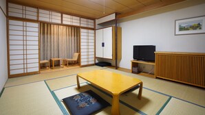 Et traditionelt japansk rum med tatamimåtter, et lavt træbord, et fjernsyn og skydedøre.