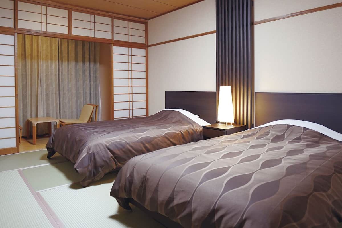 A traditional Japanese-style room with tatami flooring, two beds with matching headboards, a sliding shoji screen, and a desk with a chair.