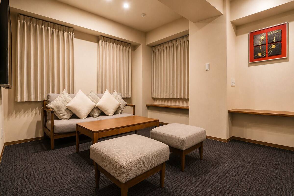 A hotel room with a sofa, ottomans, a coffee table, and a TV.