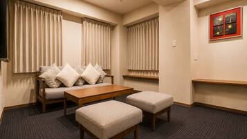 A hotel room with a sofa, ottomans, a coffee table, and a TV.