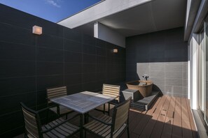 Un patio moderno al aire libre con una mesa y sillas de madera, un lavamanos integrado y una pared de azulejos oscuros.