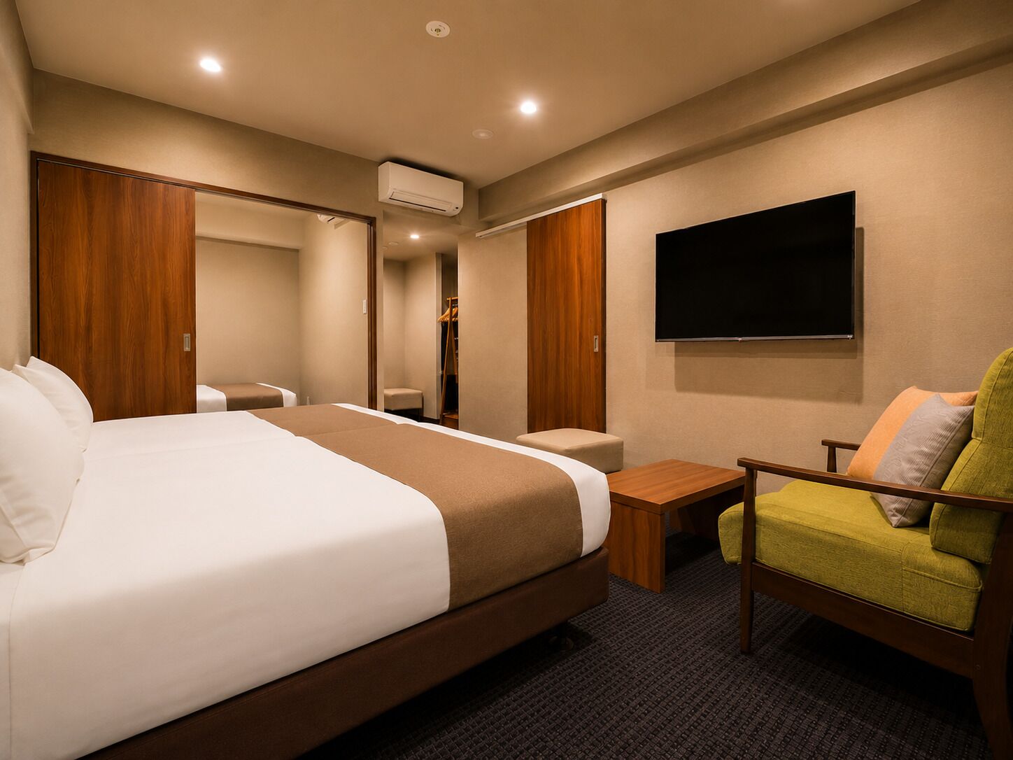 A hotel room with a large bed, a small desk, a chair, a TV, and an air conditioning unit.