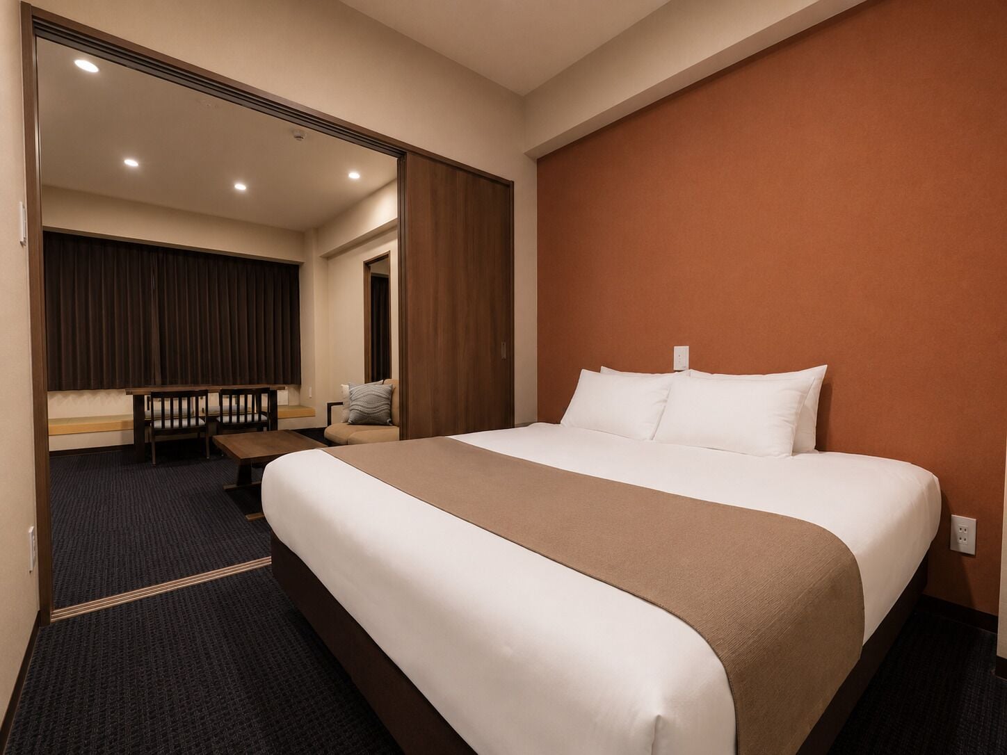 A hotel room with a large bed, a desk with a chair, a mirror, and a brown accent wall.
