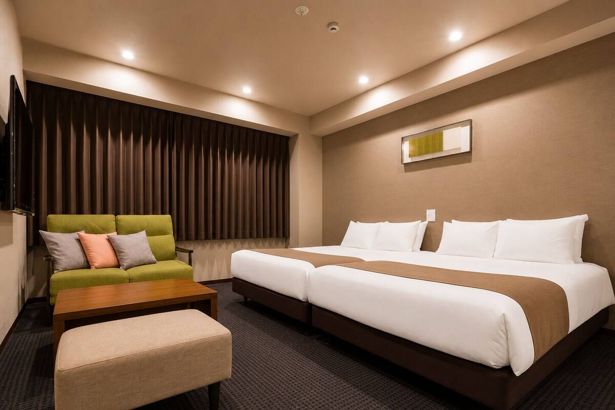 A hotel room with a green sofa, a wooden coffee table, a bench, and a double bed with white bedding.