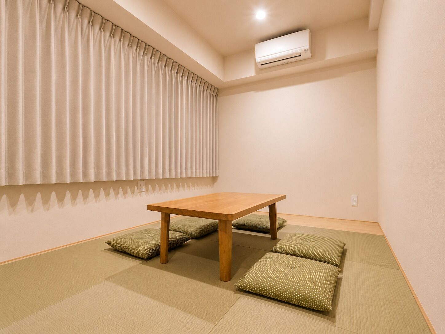 Una habitación con una mesa de madera, esteras de tatami, una ventana con cortinas y un equipo de aire acondicionado.