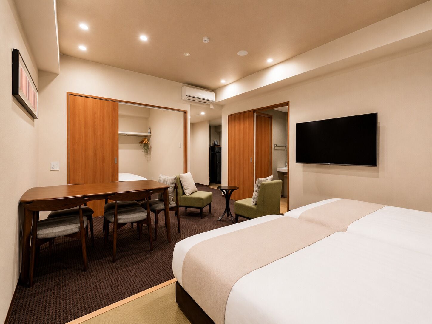 A hotel room with a bed, a desk with chairs, a TV, and a wardrobe.
