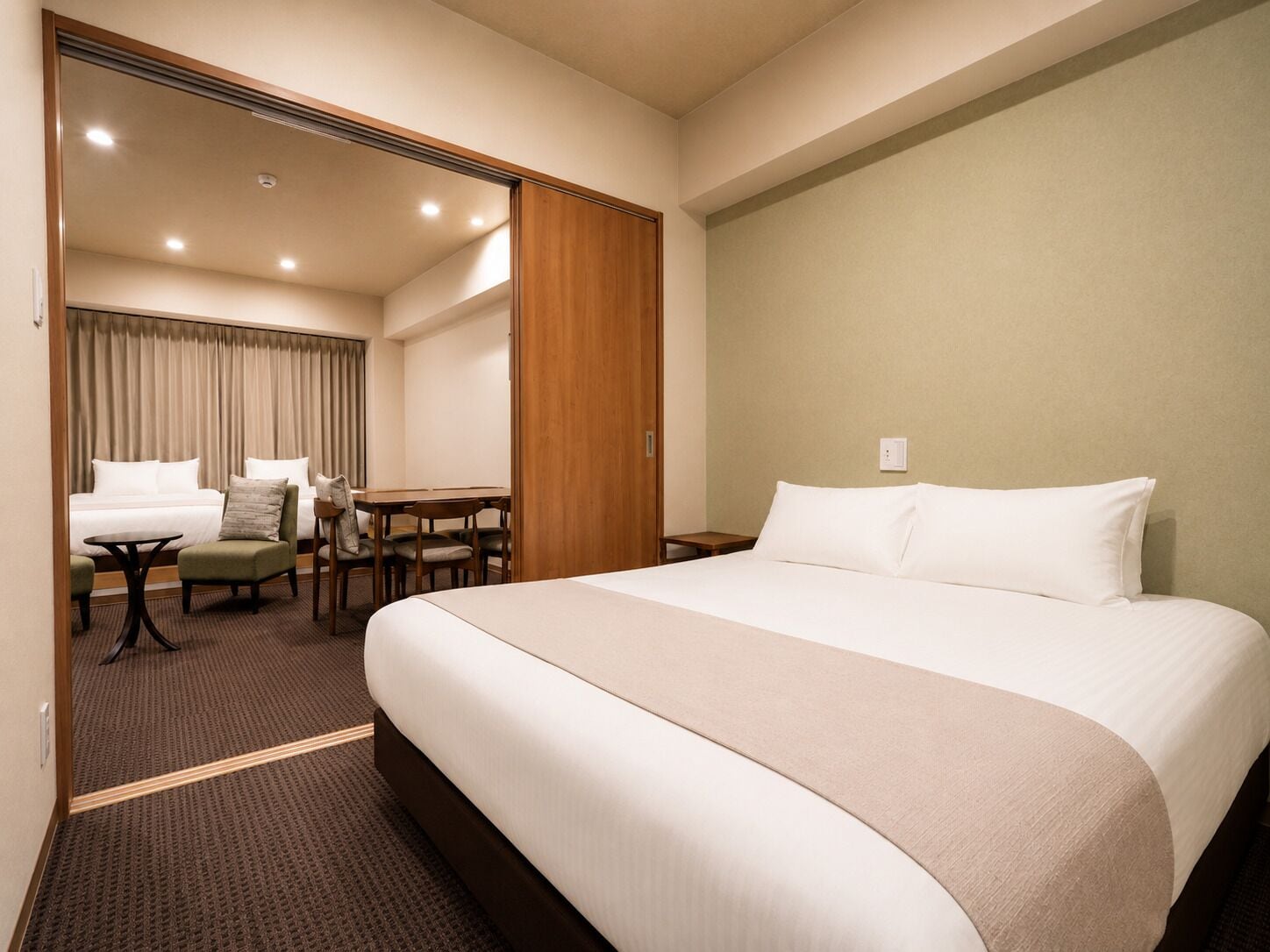 A hotel room with a large bed, a desk, two chairs, a small table, and a wardrobe.