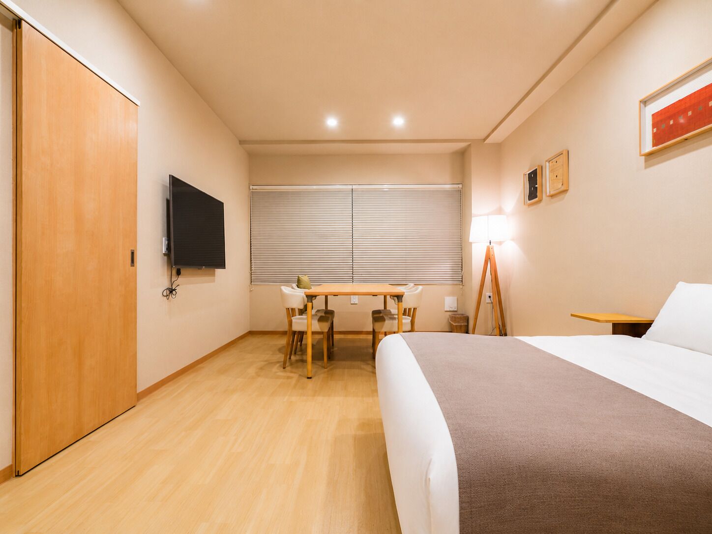 A hotel room with a bed, a desk, a chair, a television, and a window with blinds.