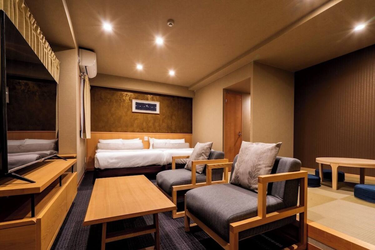 A hotel room with a bed, two sofas, a TV, a table, and a small table.