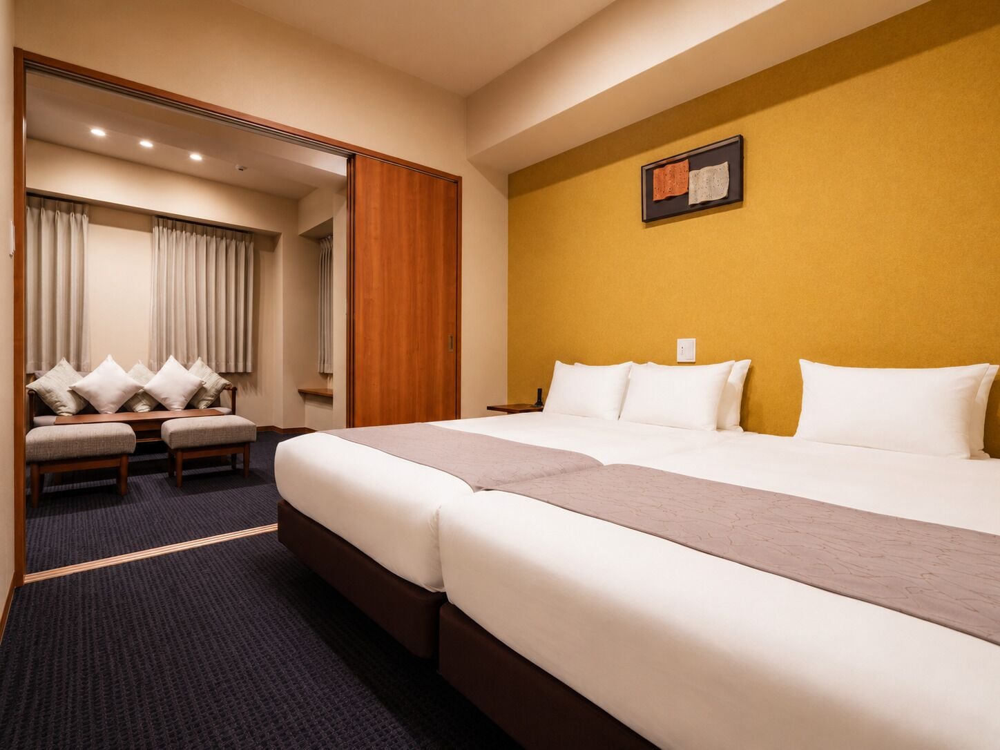 A hotel room with a large bed, a seating area with a sofa and chairs, and a wooden door.