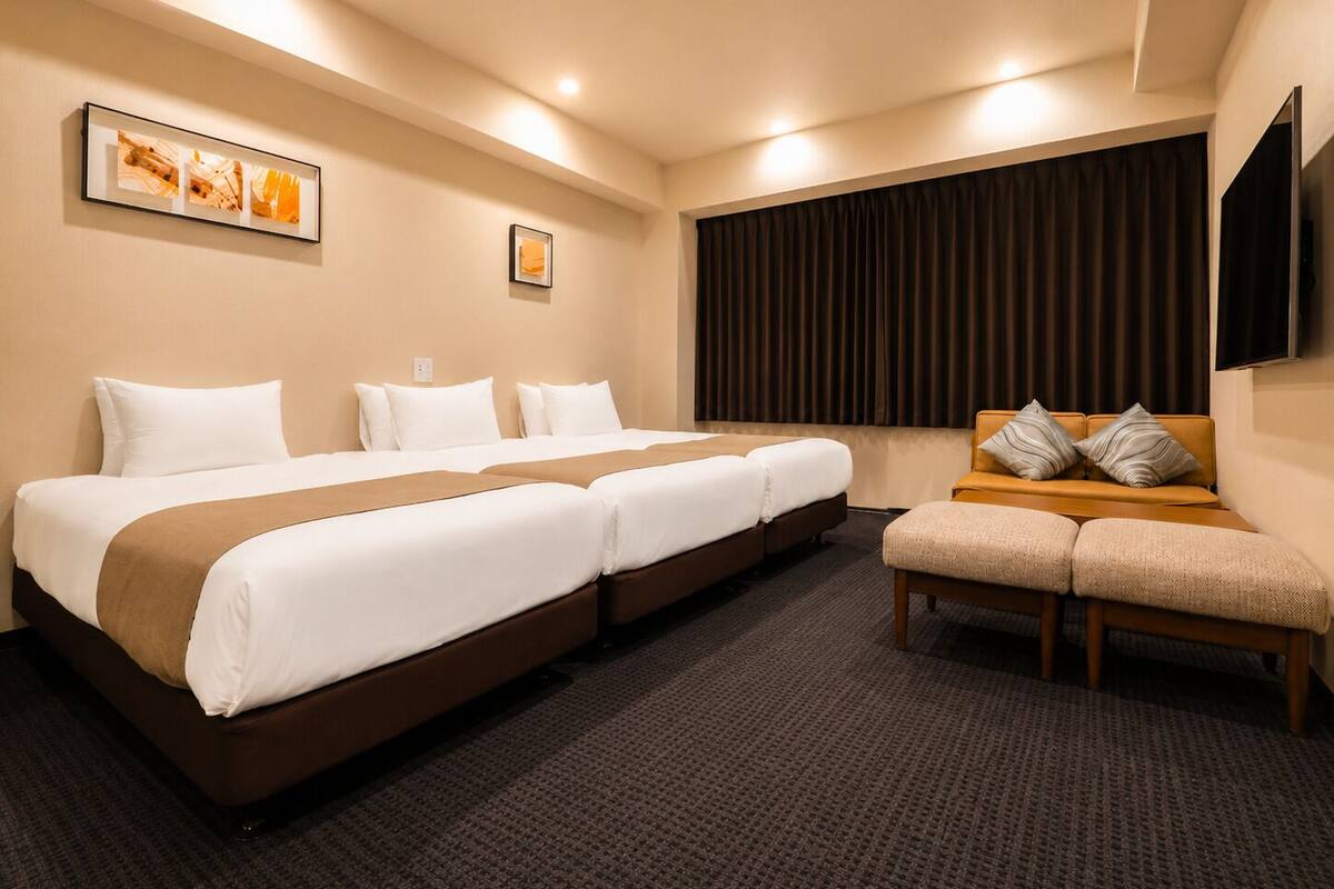 A hotel room with a large bed, a sofa, a TV, and artwork on the walls.