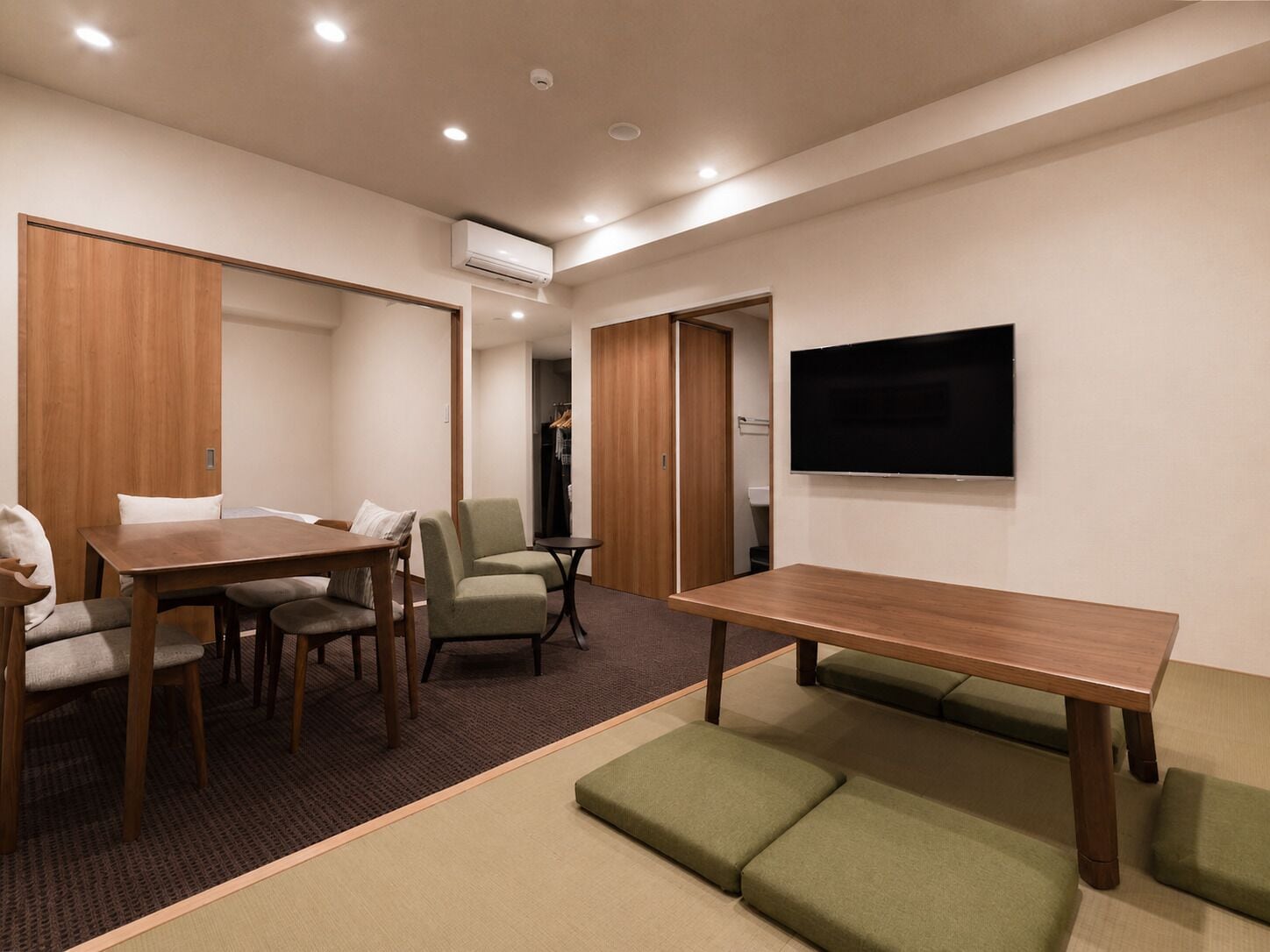 A conference room with a wooden table, chairs, a sofa, a TV, and an air conditioning unit.