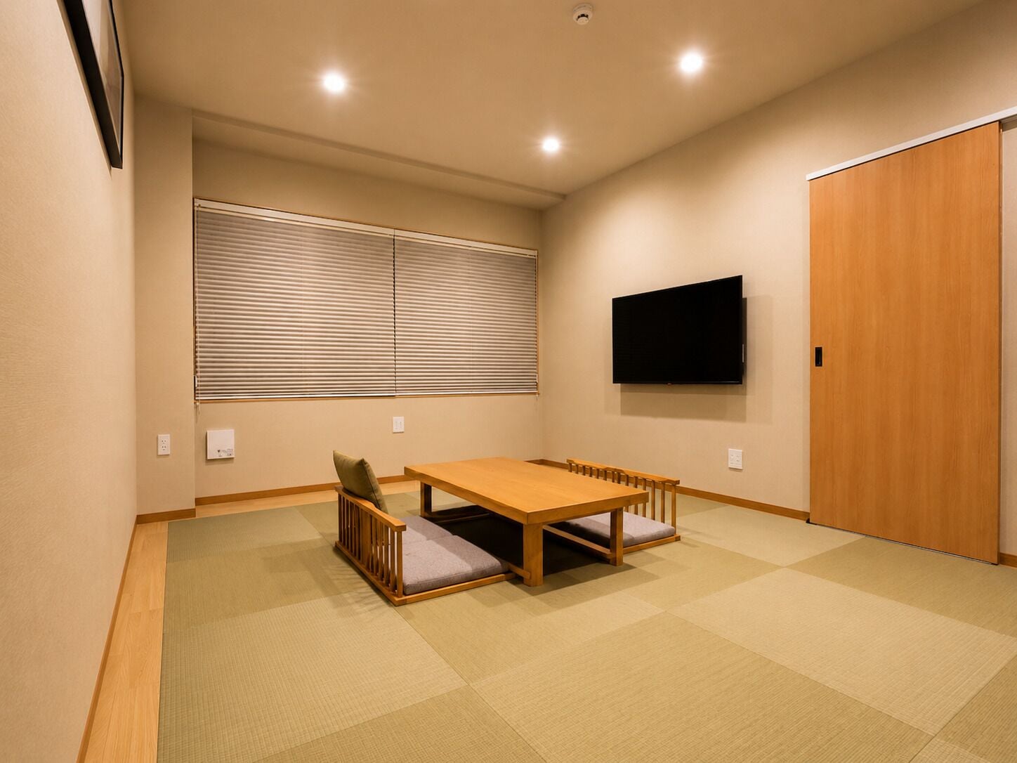 Una habitación con una mesa de madera, un sofá, un televisor montado en la pared y una puerta corrediza.