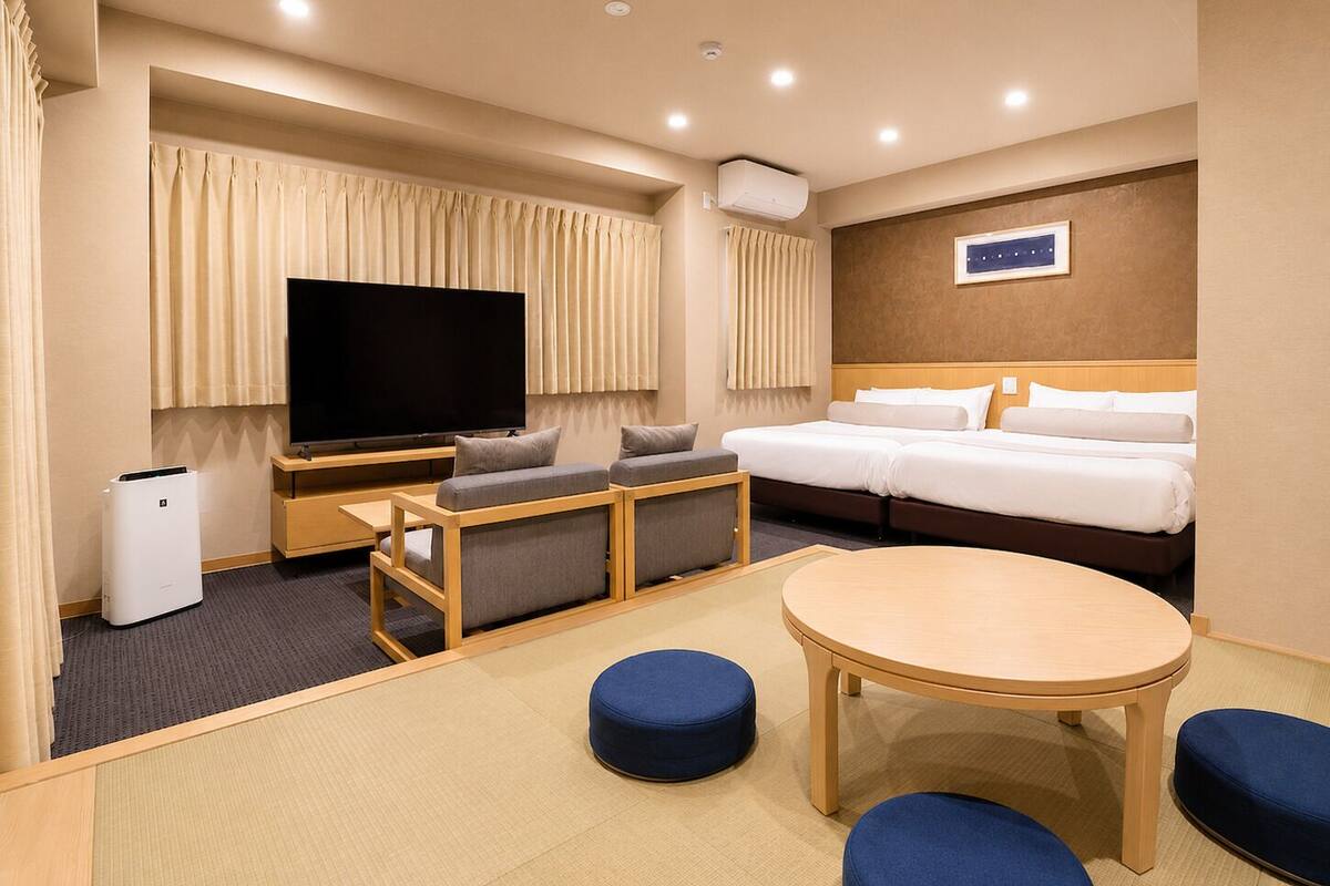 A hotel room with a bed, a TV, a seating area, and a table.