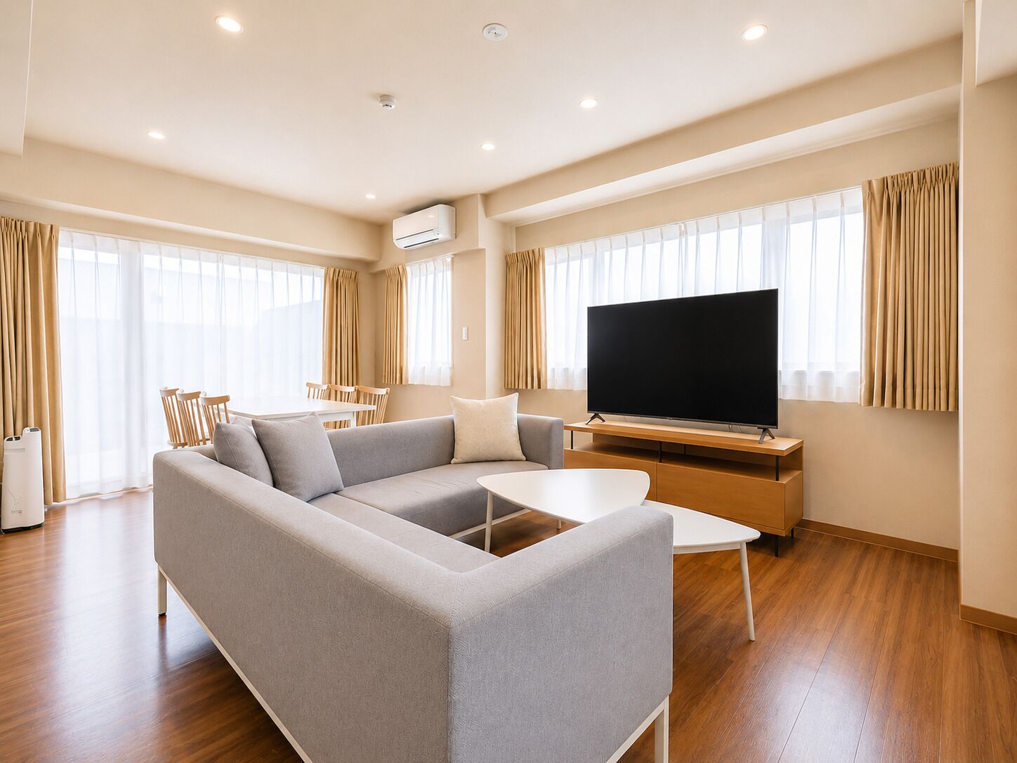 Una sala de estar moderna con un sofá seccional, un televisor de pantalla plana, una mesa de centro y una zona de comedor con sillas y una mesa.