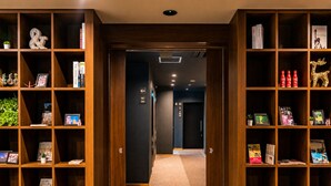 A hallway with wooden shelving units on either side, containing books, decorative items, and a sign indicating the direction to the bathroom. - Randor Residential Hotel Kyoto Suites (Kyoto)