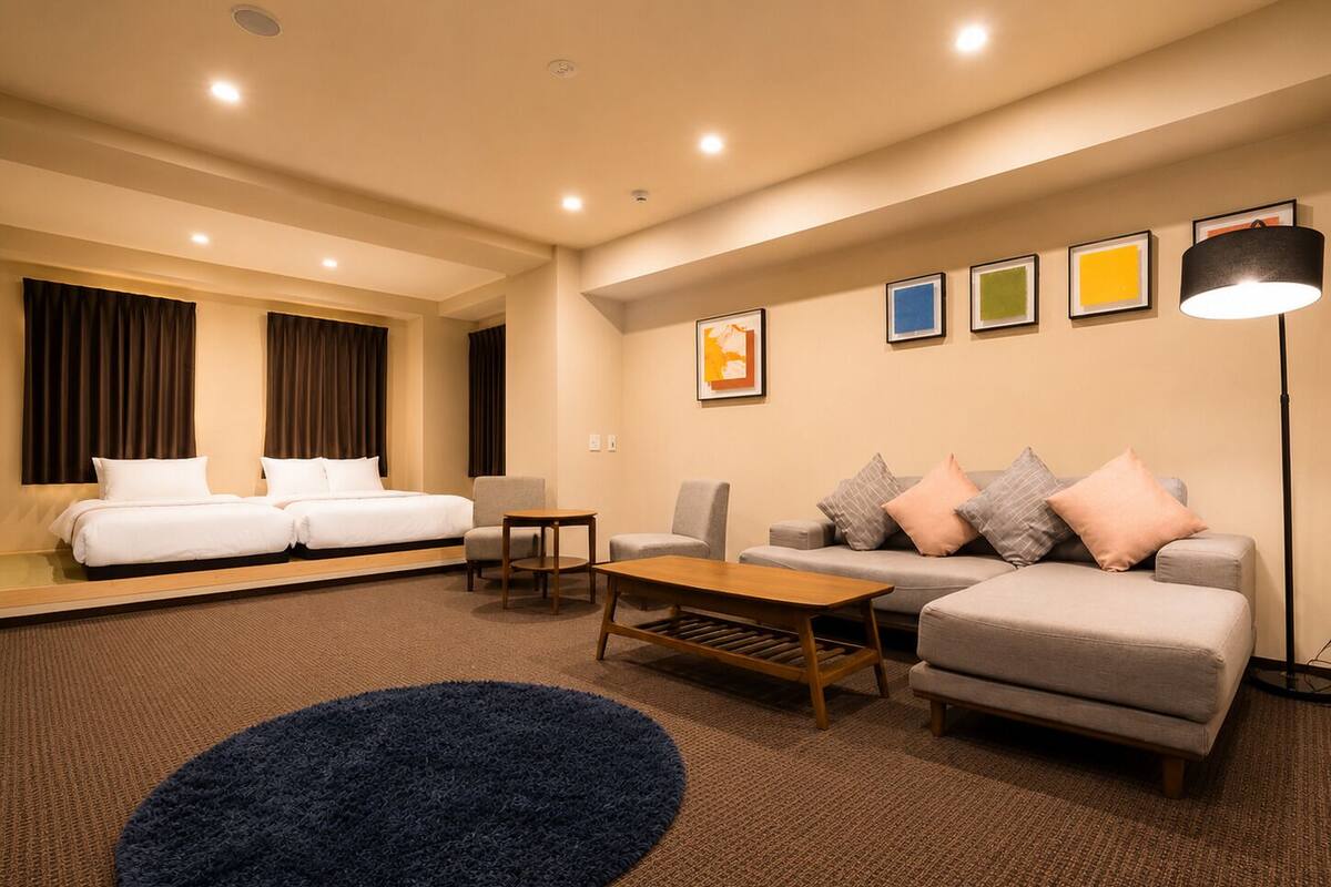 A modern hotel room with a bed, two armchairs, a sofa, a coffee table, and a large rug.