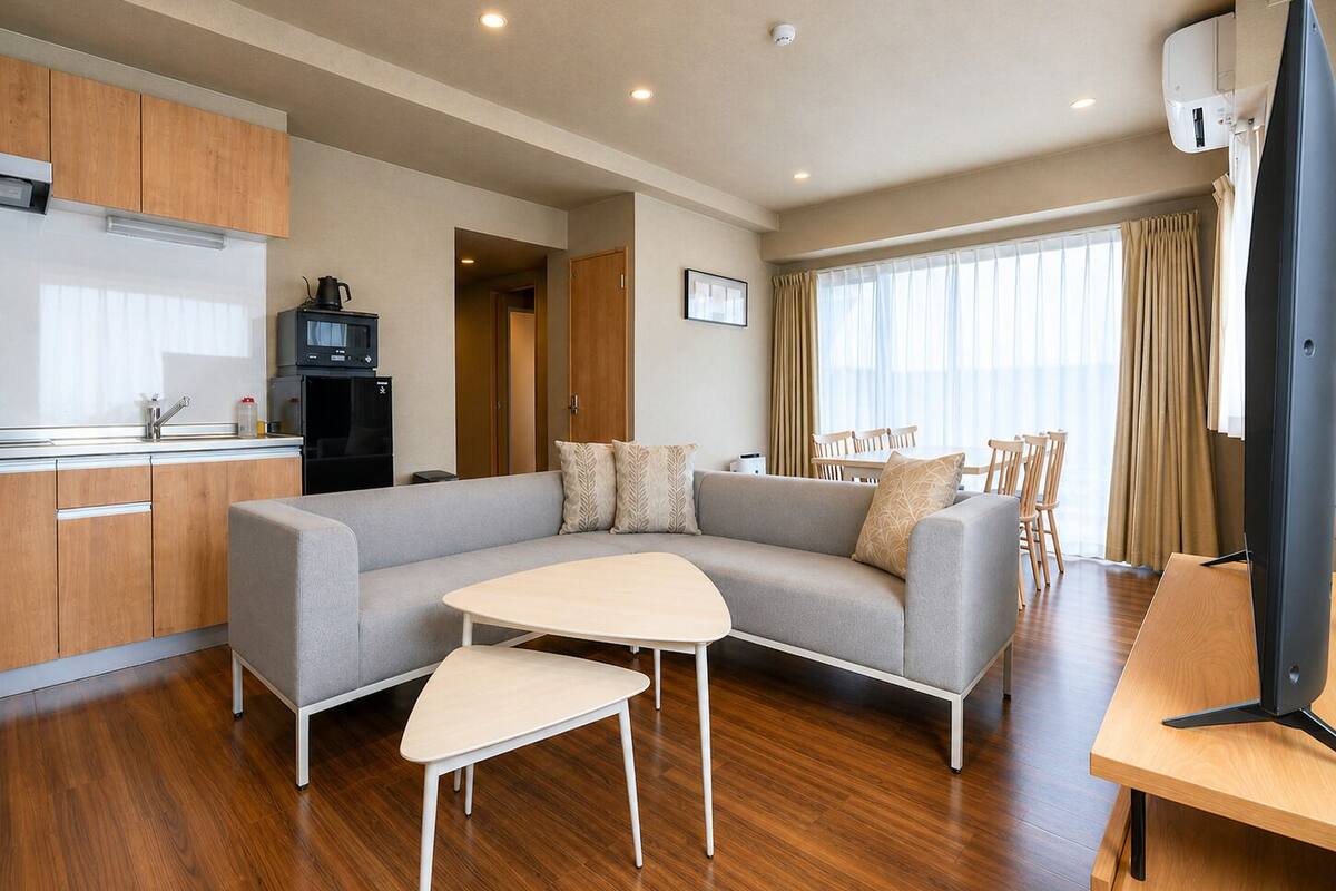 A modern living room with a sofa, a small table, a TV, and a kitchen area with cabinets and a microwave.