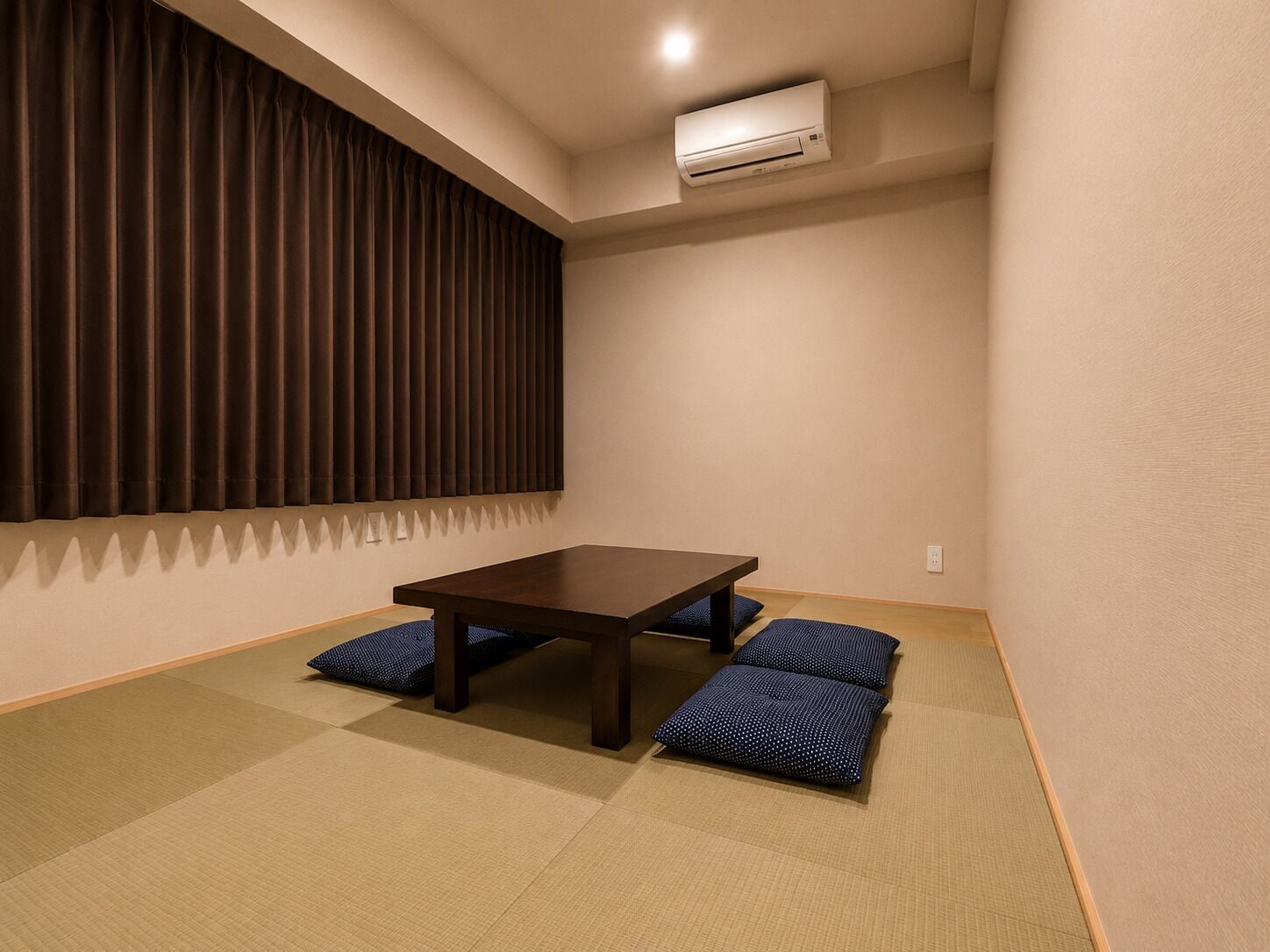 A room with tatami flooring, a low table, and a window with vertical blinds.