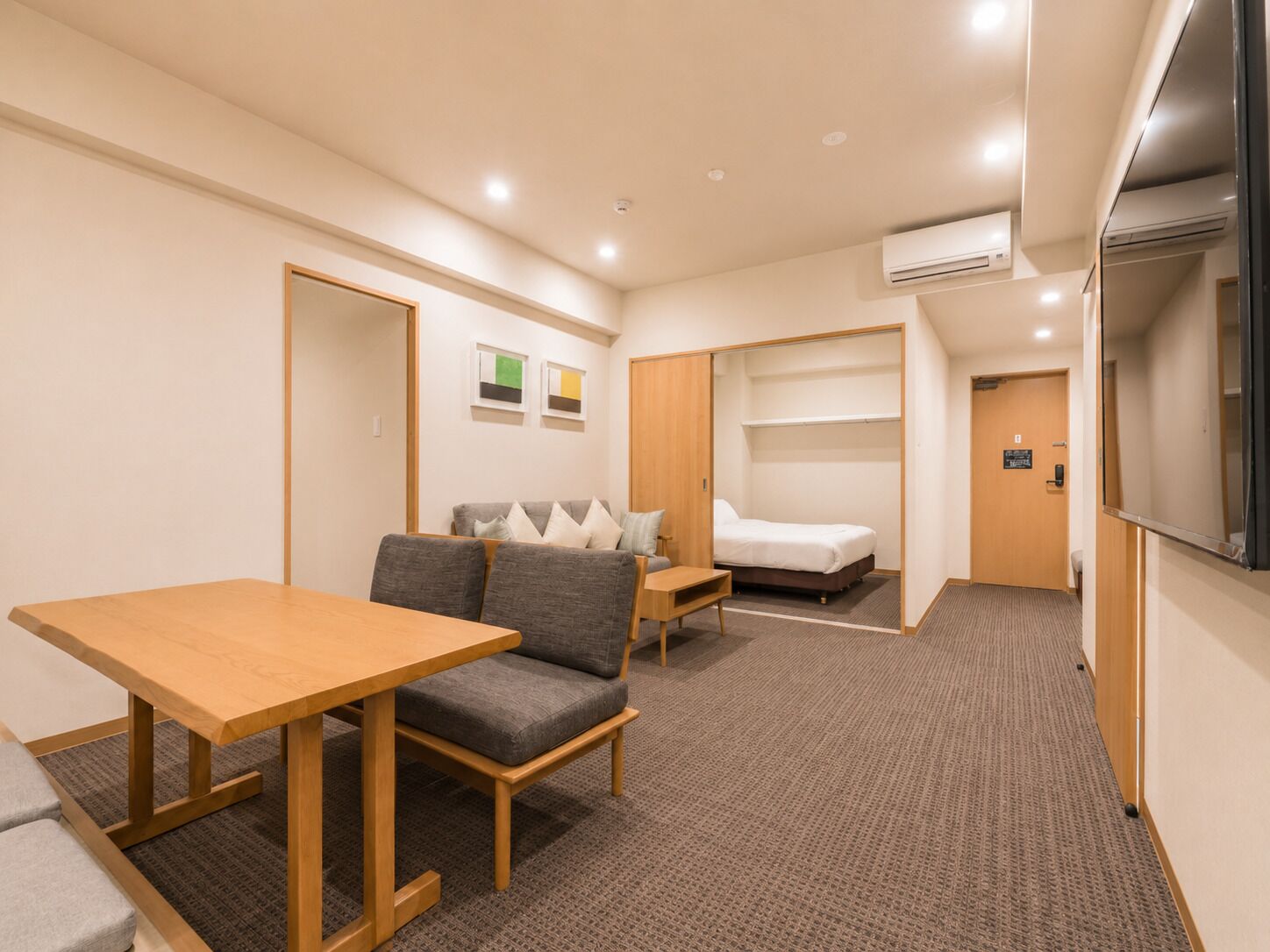 Ein Hotelzimmer mit Holztisch, Sofa, Bett und Fernseher.