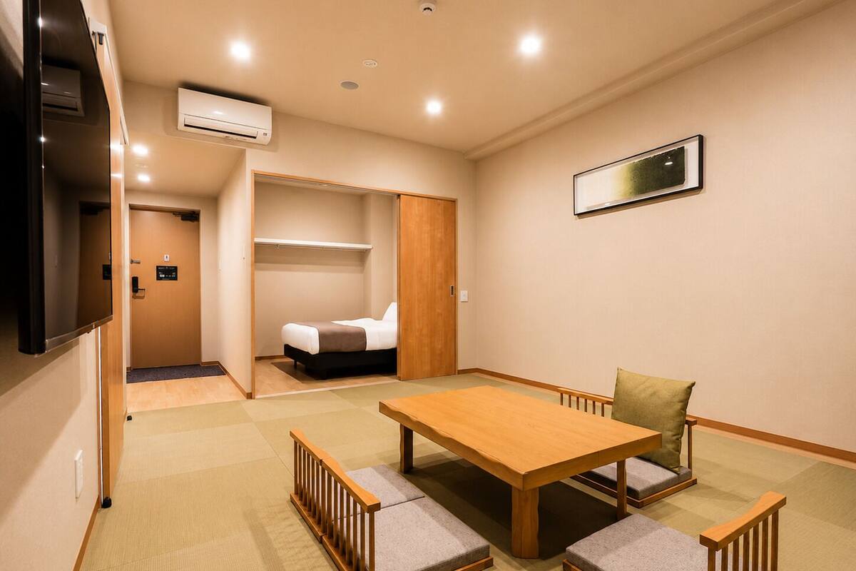 A compact hotel room with a bed, a wooden table, and a sofa.