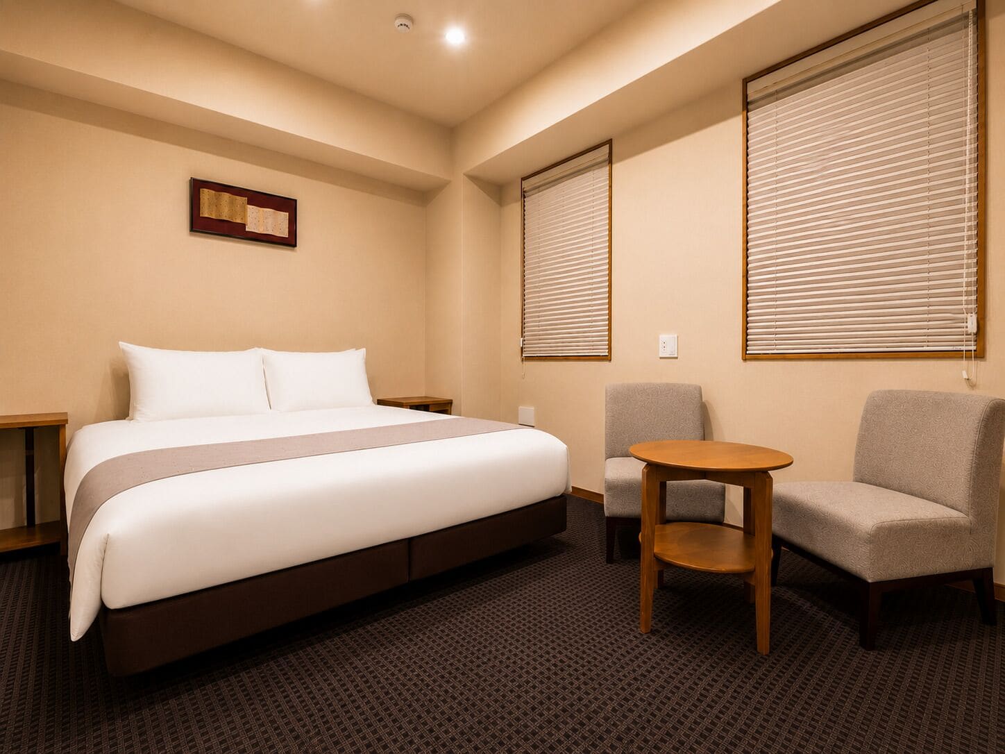 Ein Hotelzimmer mit einem Bett, zwei Sesseln, einem kleinen Holztisch und einem an der Wand hängenden Bild.