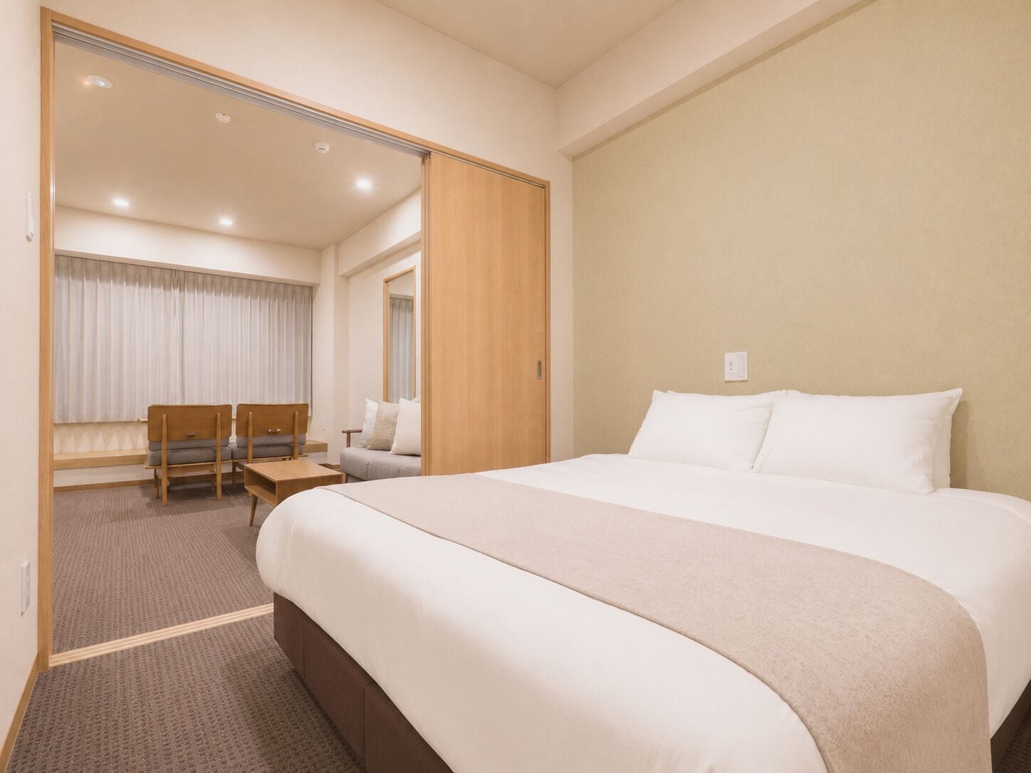 Una camera d'albergo con un letto grande, una zona salotto con divano e poltrone, un tavolino e uno specchio.