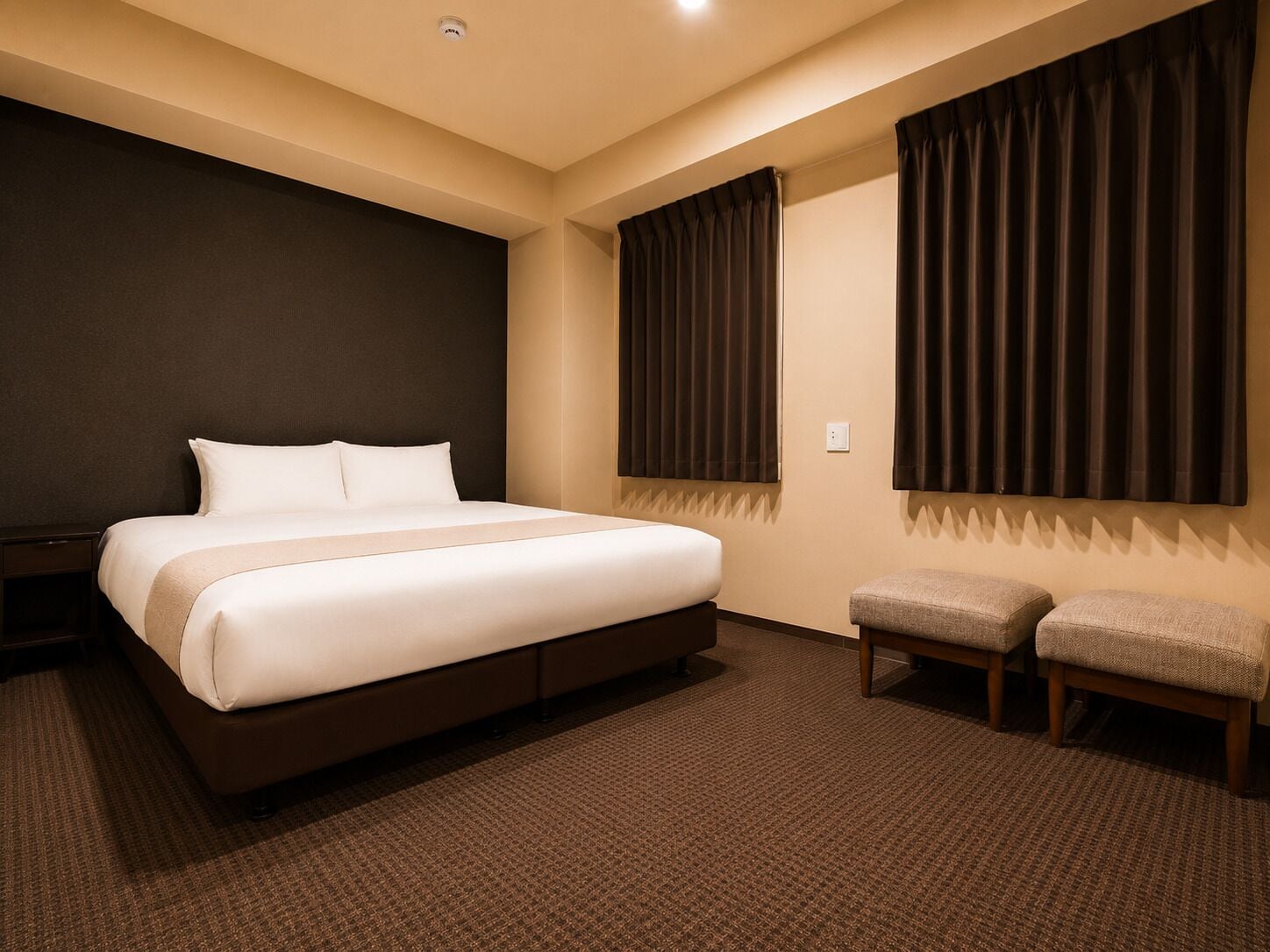 A hotel room with a large bed, two bedside tables, a small bench, and a window with curtains.
