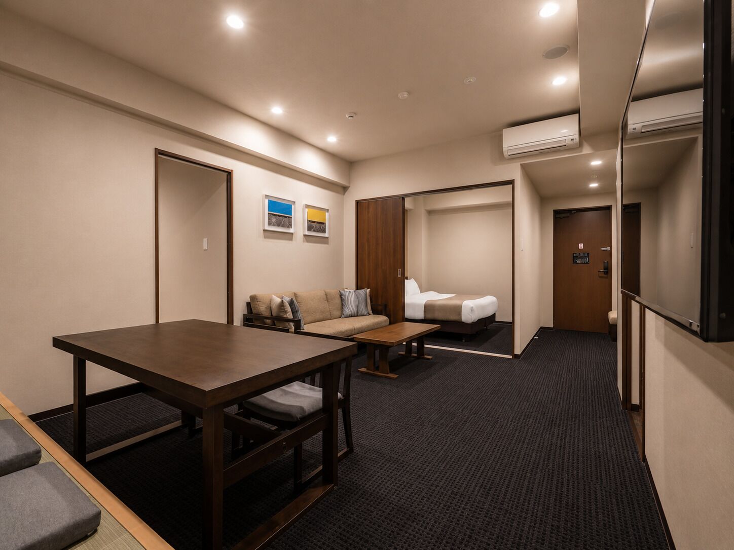 Une chambre d’hôtel avec une table en bois, un canapé, un lit et un appareil de climatisation.