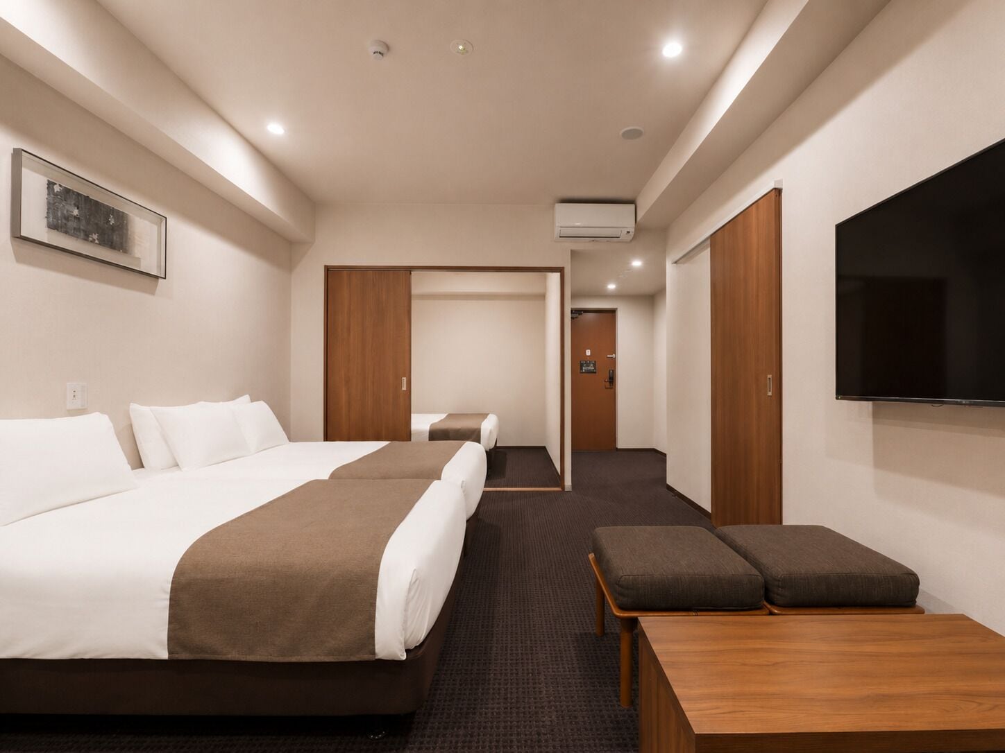 Habitación de hotel con cama, televisión, escritorio y puerta que da a un pasillo.