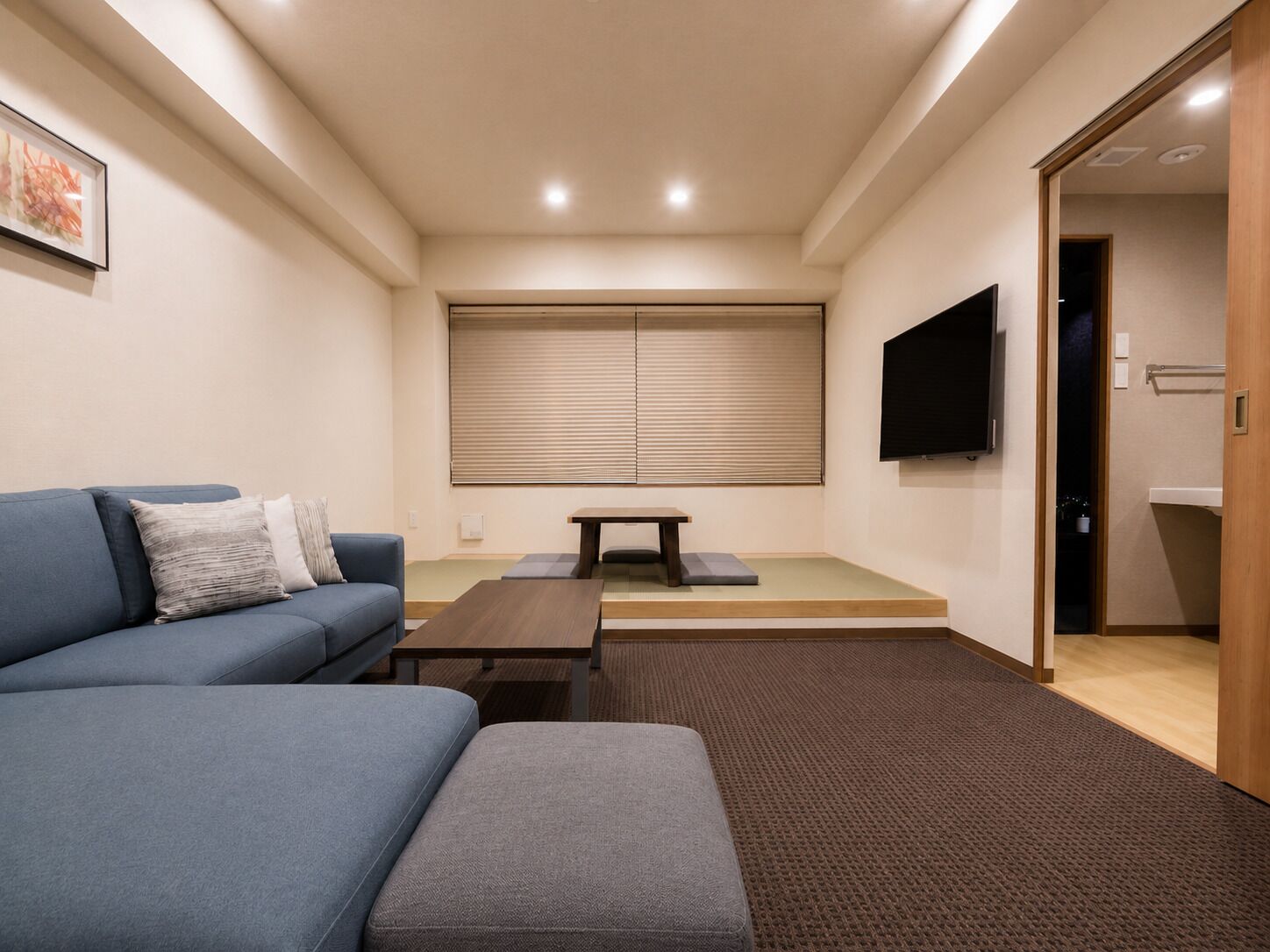 Una sala de estar con sofá, mesa de centro, televisor y puerta corredera que da a un baño.