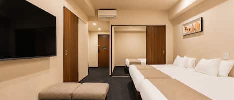 A hotel room with a TV, a desk, two beds, a sofa, and a hallway leading to another room.