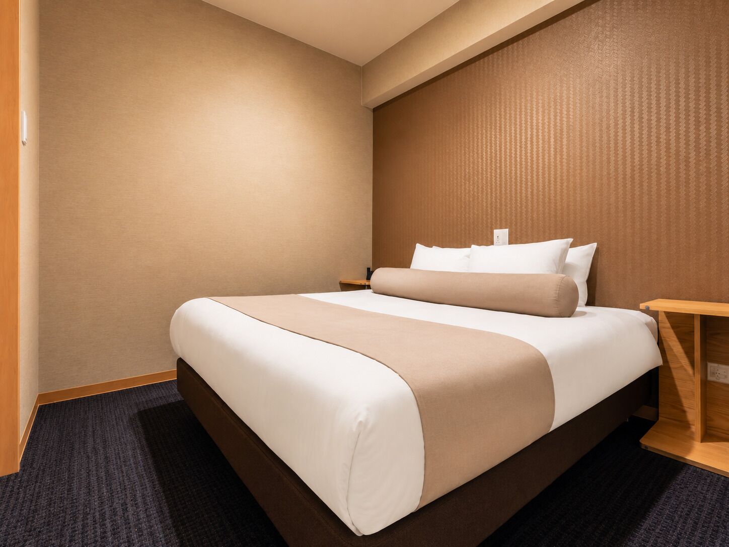 A hotel room with a bed, a nightstand, and a wooden side table.