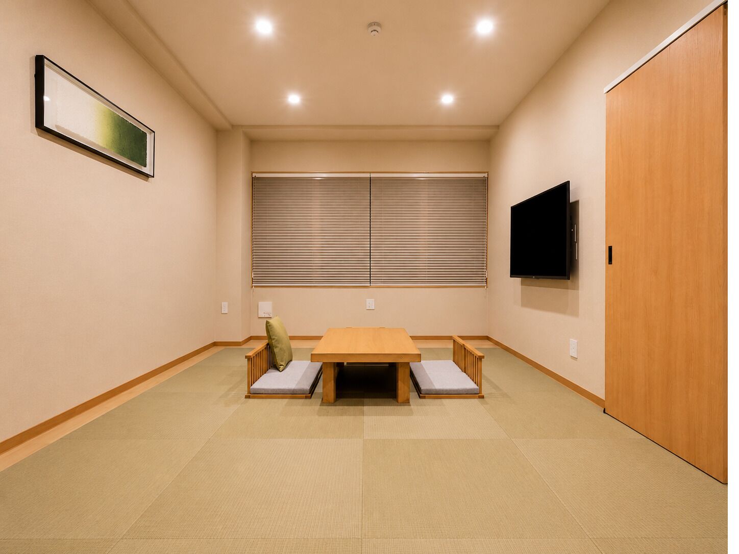 A room with tatami flooring, a low wooden table with cushions, a sliding shoji screen, a mounted TV, and a wooden wardrobe.