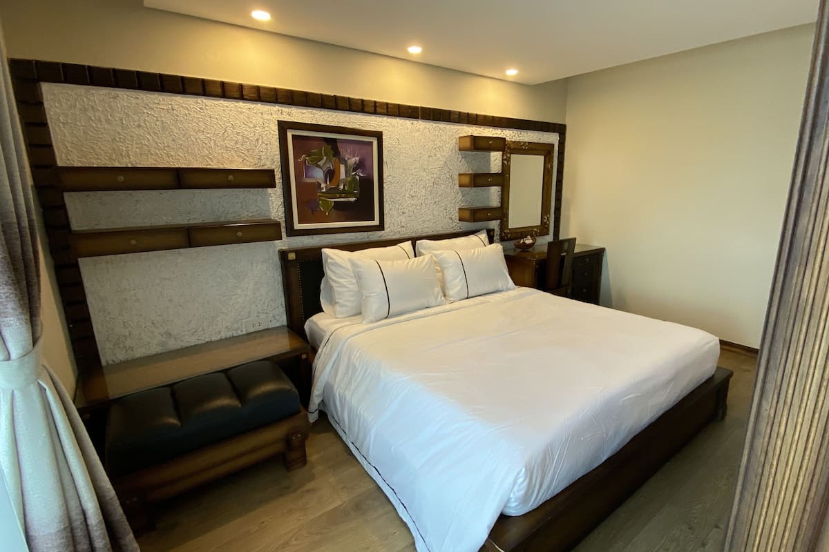 A hotel room with a large bed, a wooden headboard, a bedside table, and a wall-mounted mirror.