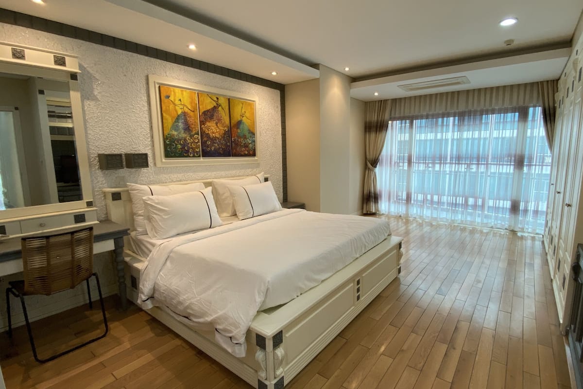 A spacious bedroom with a large bed, a bedside table, a mirror, and a painting on the wall.
