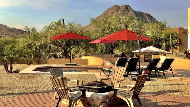 Un espace extérieur aménagé avec des chaises Adirondack et des parasols rouges, un foyer et une vue sur une montagne.