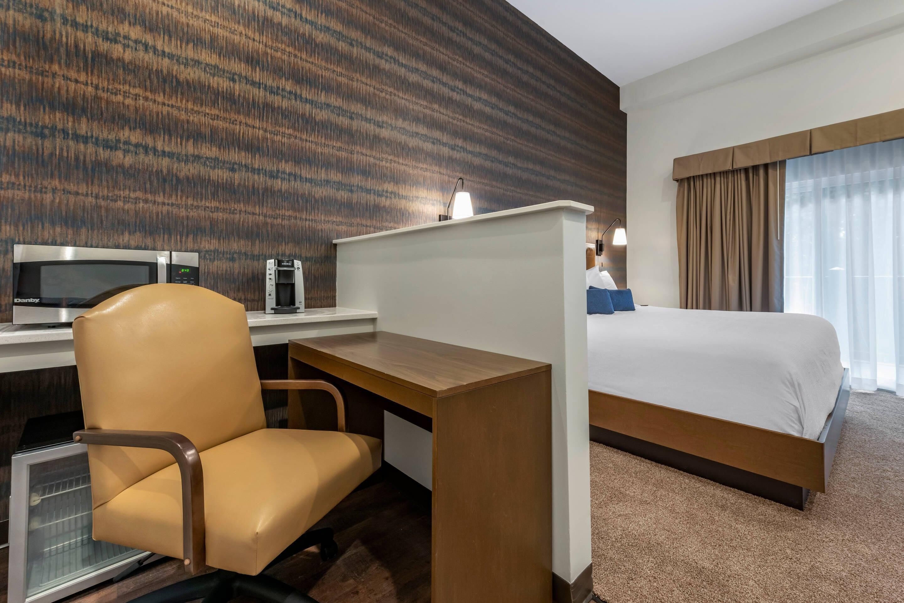 A hotel room with a bed, a desk with a chair, a microwave, and a TV.