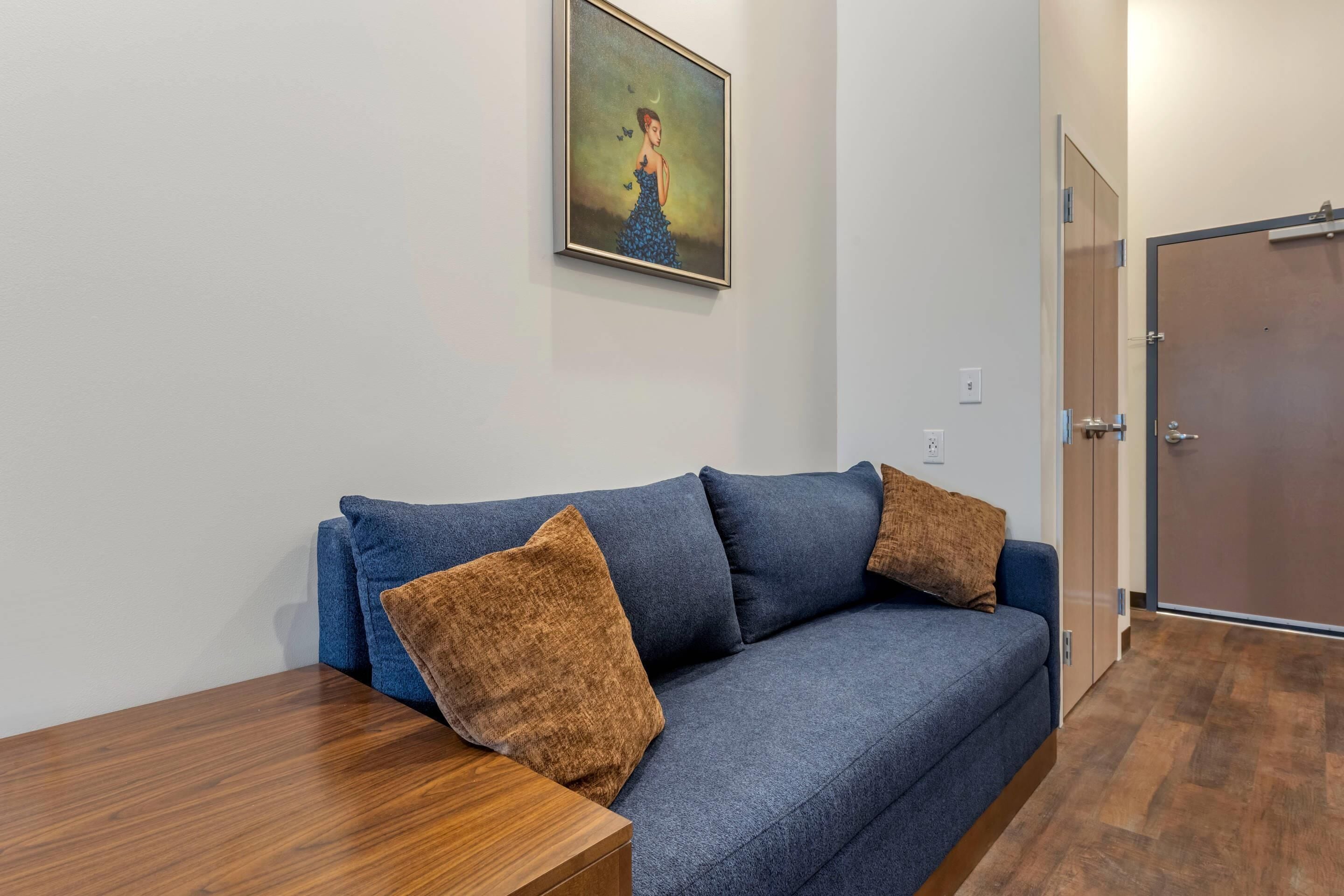A room with a blue sofa, a wooden table, and a painting on the wall.