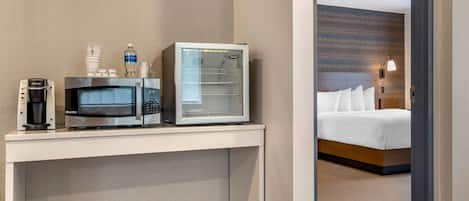 A hotel room with a bed, a desk with a microwave, a coffee maker, and a bottle of water.