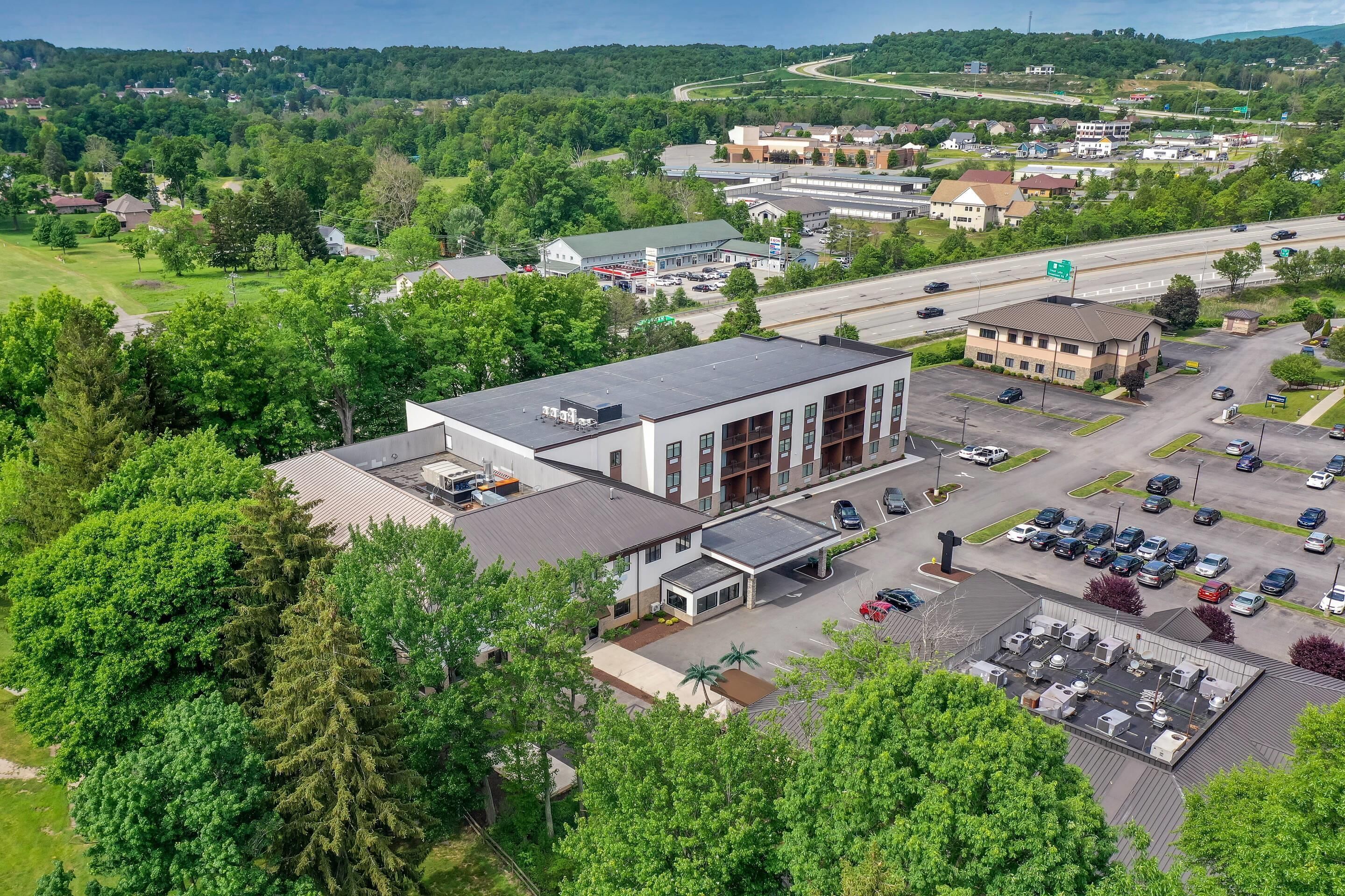 An aerial view of a commercial building with a parking lot, surrounded by greenery and other buildings.