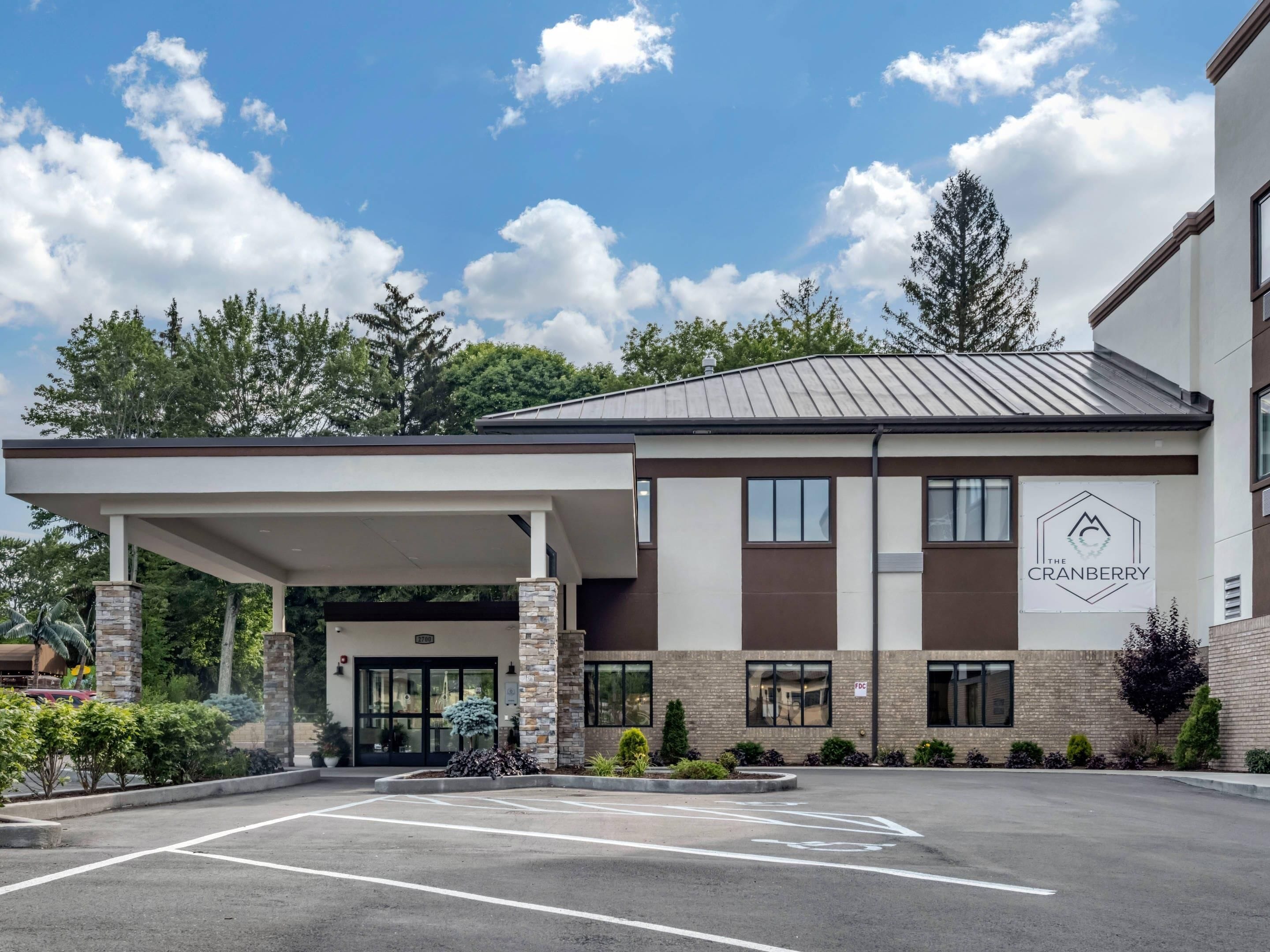 A modern building with a covered entrance, a parking lot, and a sign reading "The Cranberry."